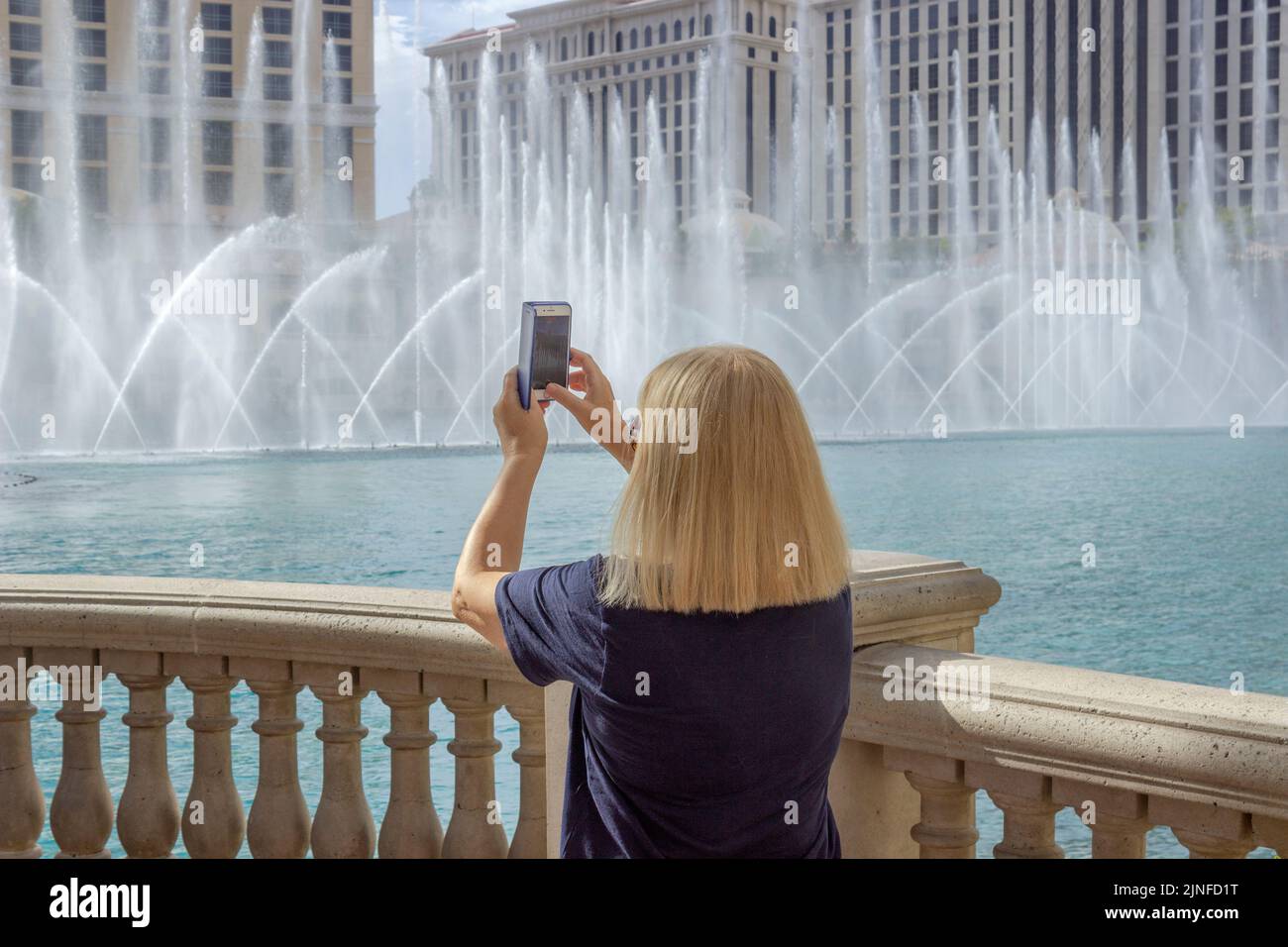A woman taking vertical pictures with a cell phone of the water fountains at Bellagio Las Vegas Stock Photo