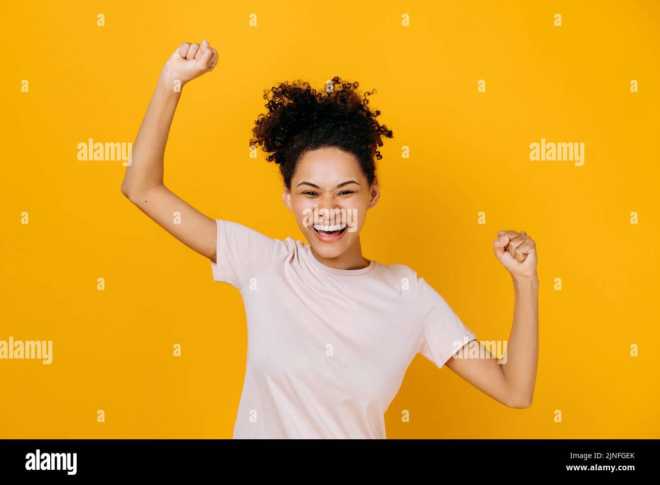 Good news, success and happiness concept. Excited happy curly-haired african american woman, dancing, gesturing with fists, receives profit, glad to win lottery, standing on isolated orange background Stock Photo