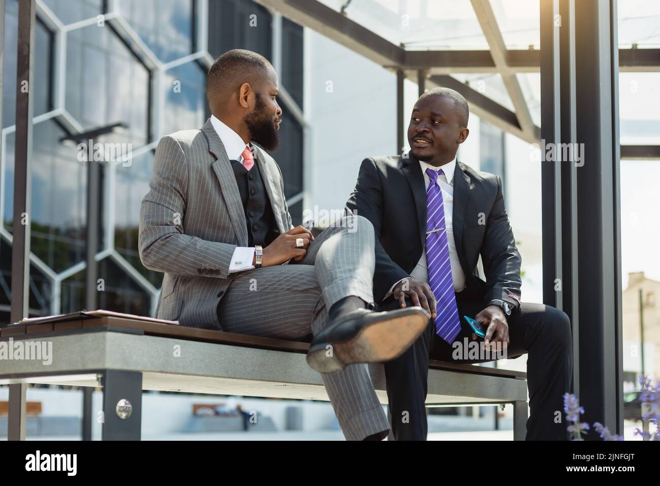 Business meeting of friends outdoors. Two dark-skinned men in suits are ...