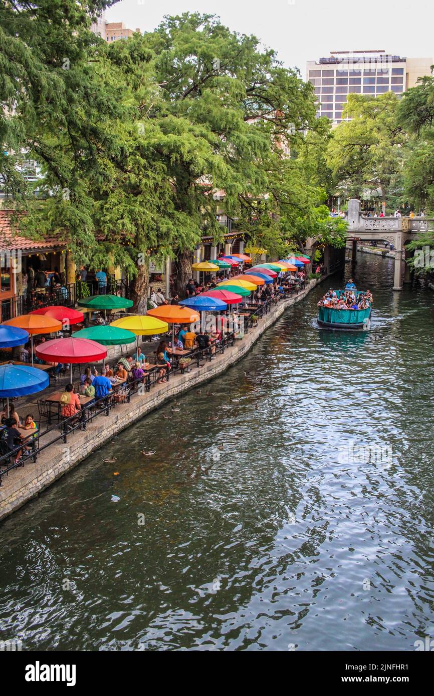 A tour boat sailing past colorful umbrellas along the river walk in San Antonio Texas. Stock Photo