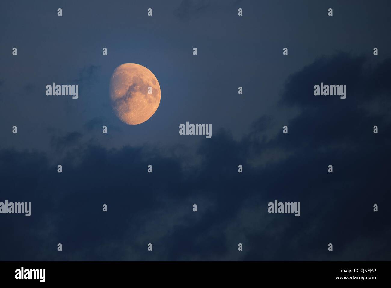 Bright orange moon against dark sky and clouds Stock Photo