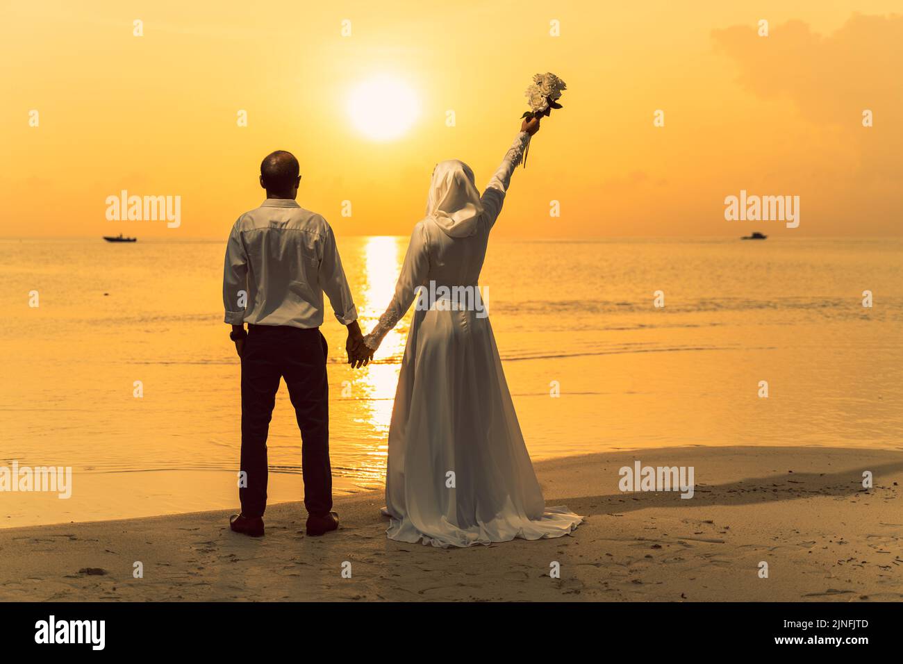 A beautiful couple meets the sunset on the seashore. Newlyweds in rays of the golden sun Stock Photo