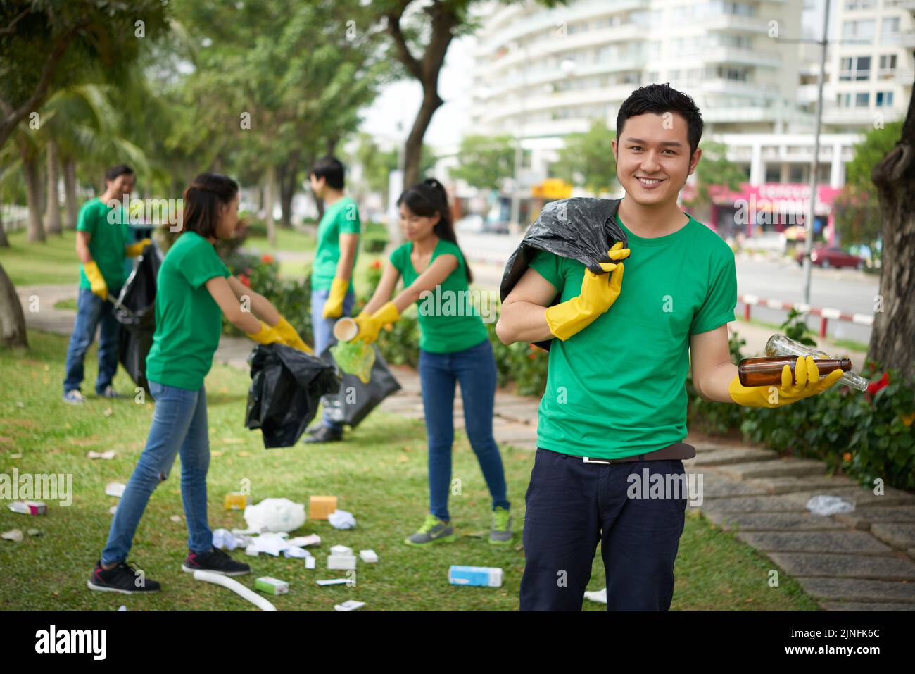 Handsome smiling Asian man picking up litter into plastic bag during neighborhood cleanup Stock Photo