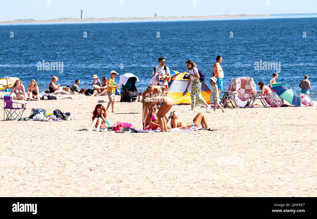 Dundee, Tayside, Scotland, UK. 11th Aug, 2022. UK weather: Extremely hot August temperatures in North East Scotland reached 28°C. Visitors swarm to Broughty Ferry beach in Dundee to enjoy the warm, wonderful summer weather and sunbathe on the sand. Stunning woman enjoying themselves while being photographed sunbathing. Credit: Dundee Photographics/Alamy Live News Stock Photo