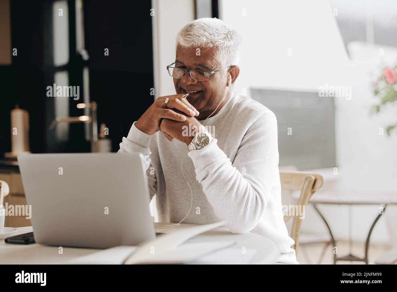 Happy senior businessman attending an online meeting in his home office. Mature businessman having a video conference with his colleagues while workin Stock Photo