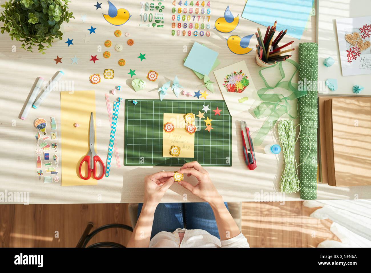 Creative woman gluing paper flowers on handmade greeting card while