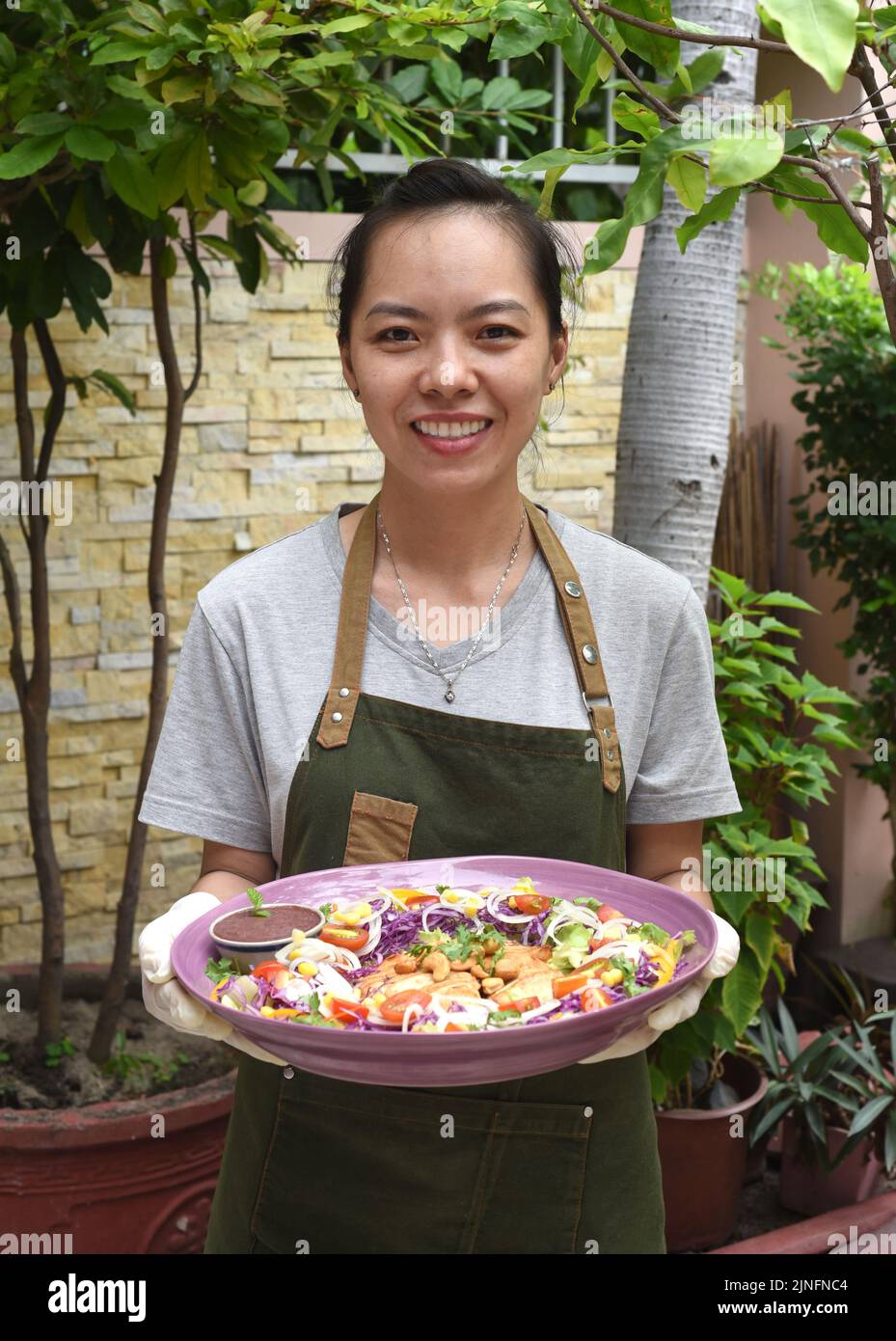 Vietnamese woman waitress serving pan fried chicken with vegetables in outdoor cafe Stock Photo