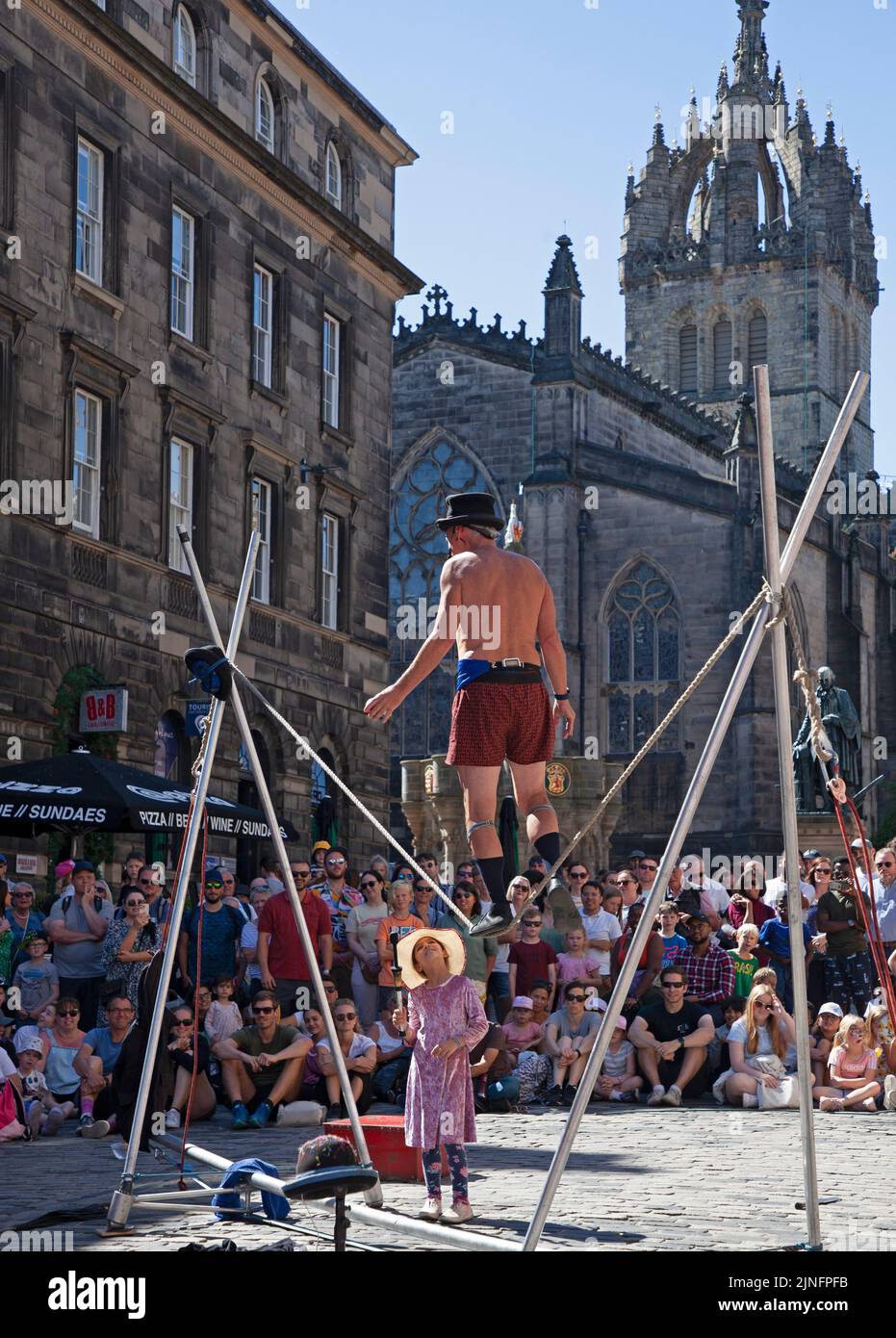 City Centre, Edinburgh, Scotland, UK. 11th August 2022. EdFringe 6th Day on the Royal Mile keeping busy with crowds of people looking for entertainment. Weather 27 degrees centigrade had people looking to top up water bottles and to find shade in the ciy's gardens. Pictured: Kwabana Lindsay on a slack rope interacting with a small girl from the audience. Credit: Arch White/alamy live news. Stock Photo