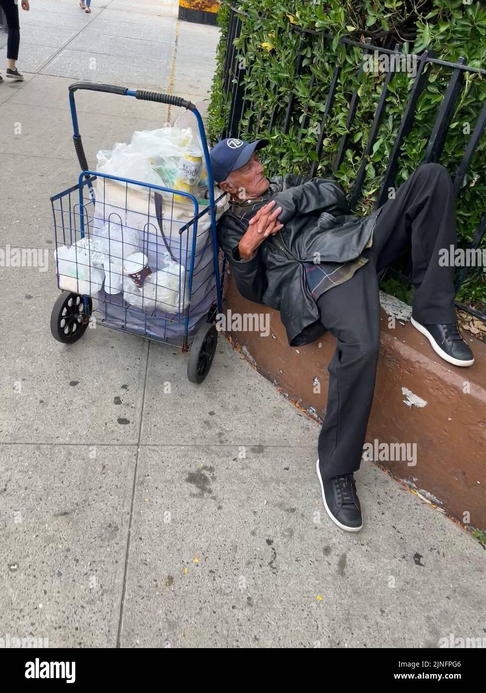 Man sleeps along a fence on a sidewalk on a very hot summer day in the Park Slope neighborhood of Brooklyn, New York. Stock Photo