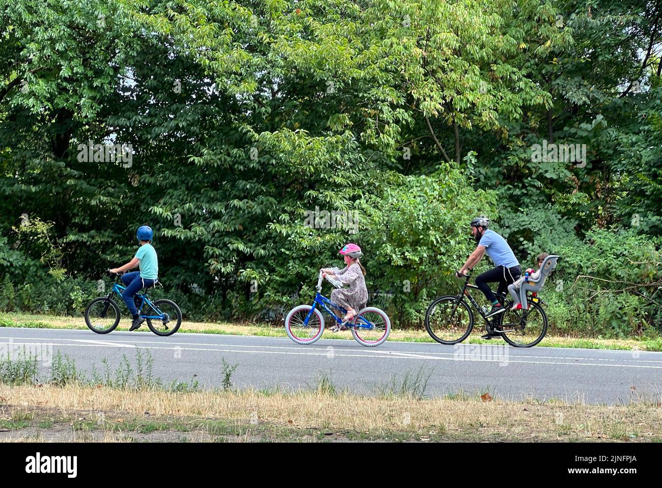 Dad with kids riding bicycles on the road in Prospect Park, Brooklyn, New York. Stock Photo