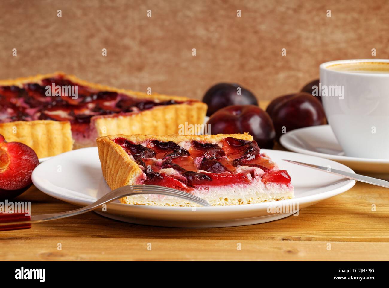 Closeup piece of homemade plum cake and cup of coffee on wooden table. Shallow focus. Stock Photo