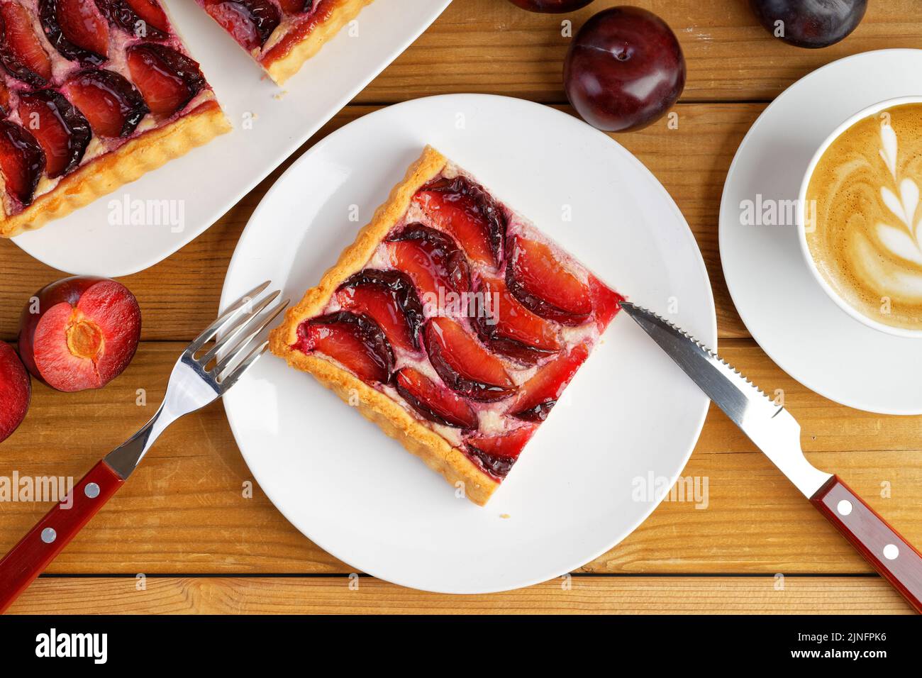 Closeup piece of homemade plum cake and cup of coffee cappuccino on wooden table. Top view. Stock Photo