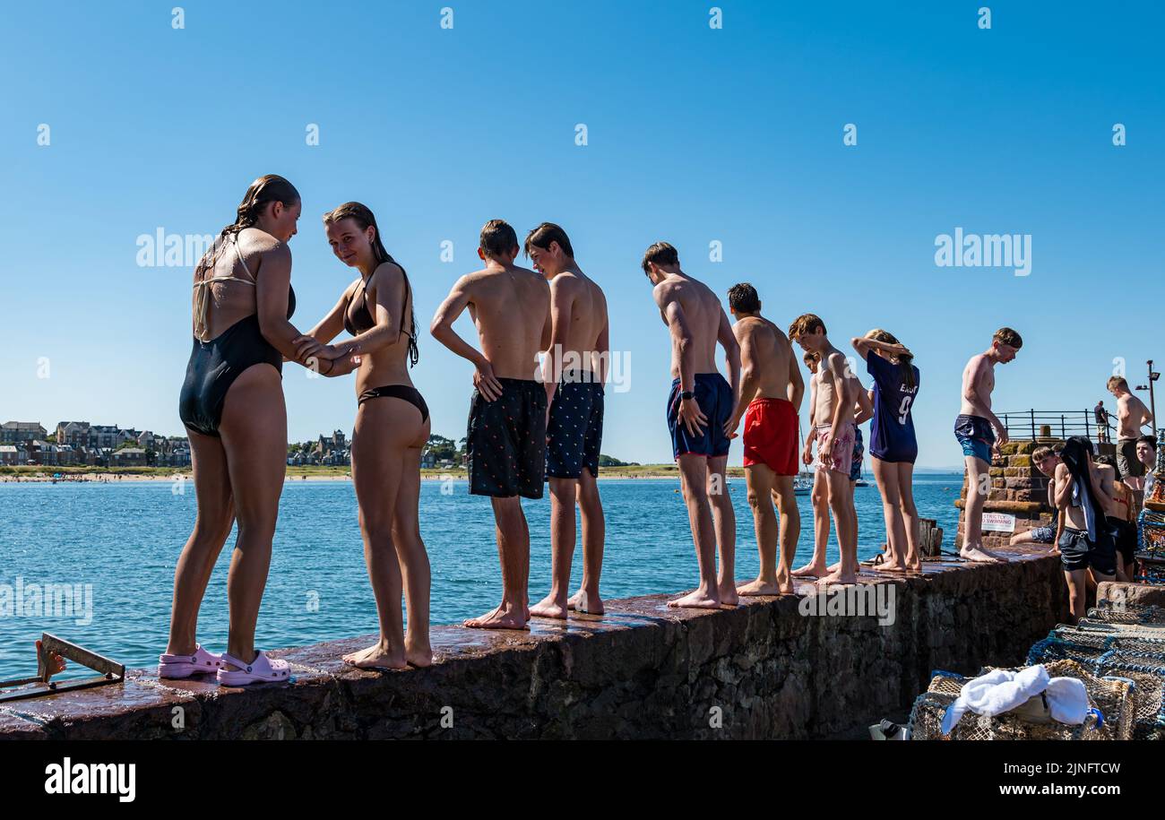 North Berwick, East Lothian, Scotland, UK, 11th August 2022. UK Weather: Keeping cool in the heat. With the temperature reaching up to 27 degrees, the seaside town offers opportunities to cool down. Children wearing swimsuits line up standing on the harbour wall in the Summer heatwave weather ready to jump into the sea Stock Photo
