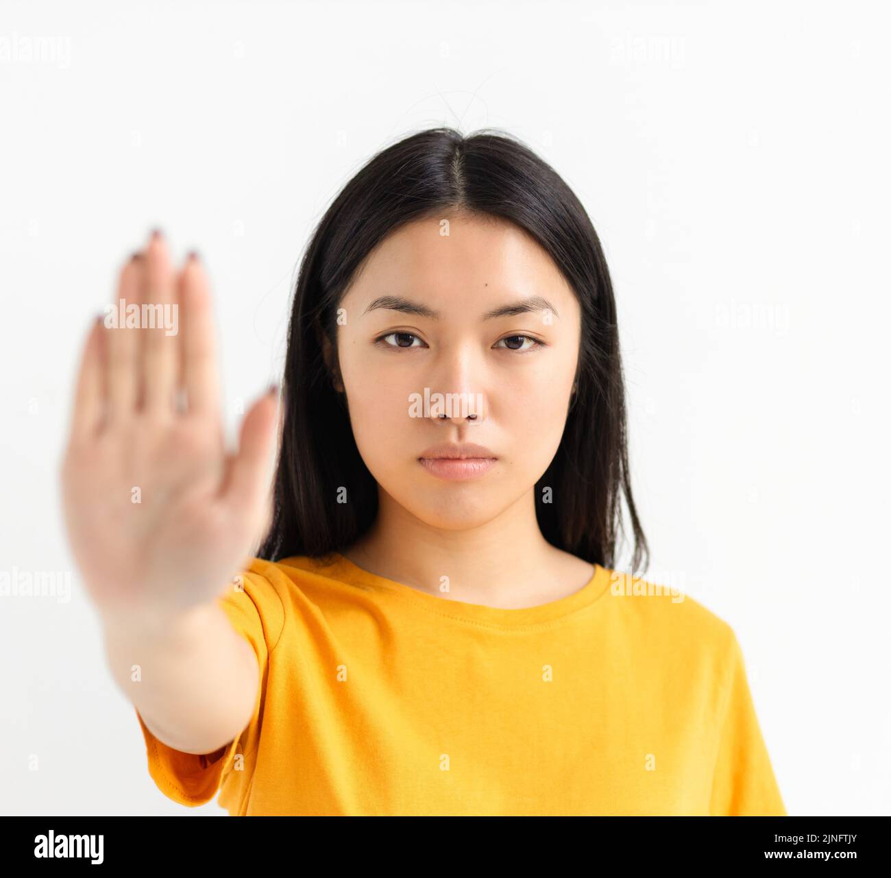 Portrait of young serious Asian woman showing stop gesture and looking at camera on white background Stock Photo