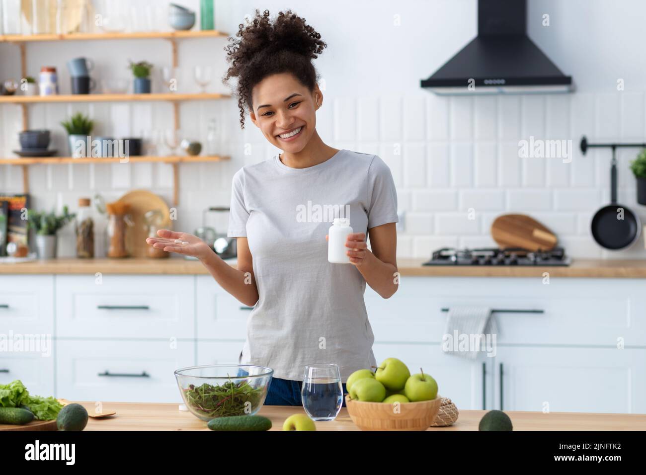 Happy african american woman in home kitchen holding bottle of nutritional supplements Stock Photo