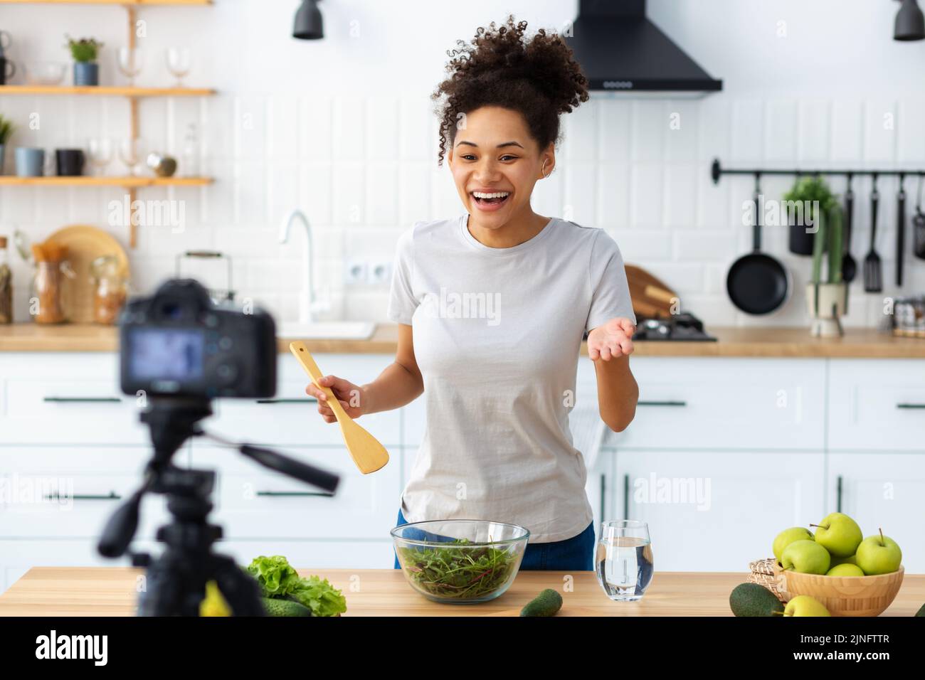 young female preparing salad in home kitchen Beautiful woman using camera to record video of cooking healthy food Stock Photo