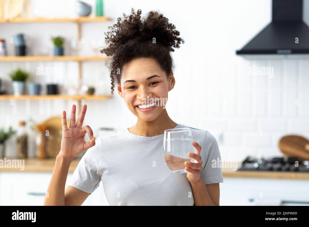 Healthy lifestyle Young woman holding glass of fresh clean water looks at camera smiles friendly Stock Photo