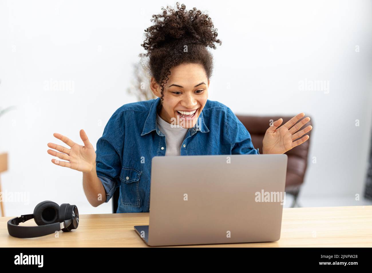 excited young African American woman celebrating success sitting with laptop at home or office Stock Photo