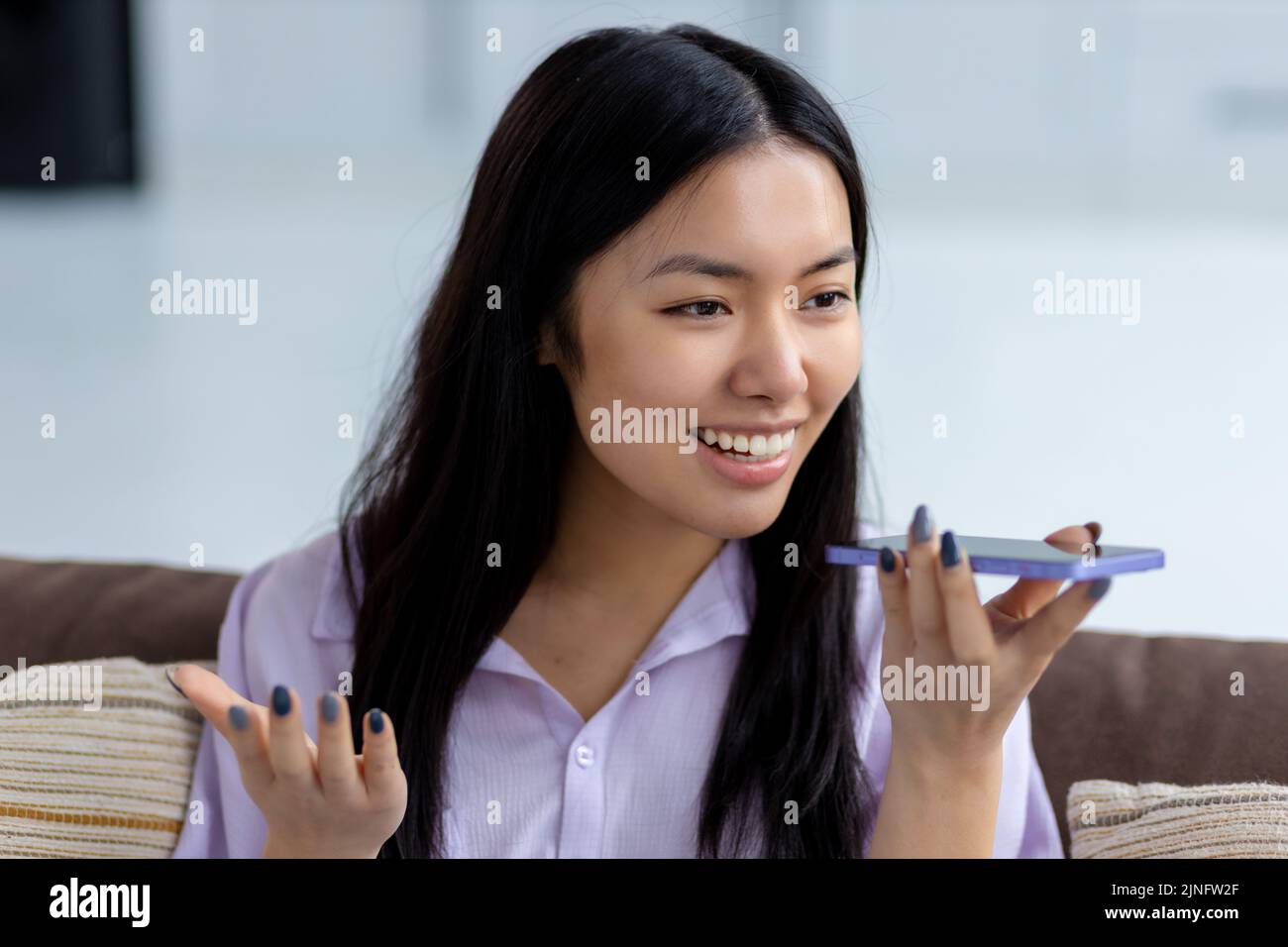 Young Asian woman sending voice message through using mobile phone smiling friendly Stock Photo
