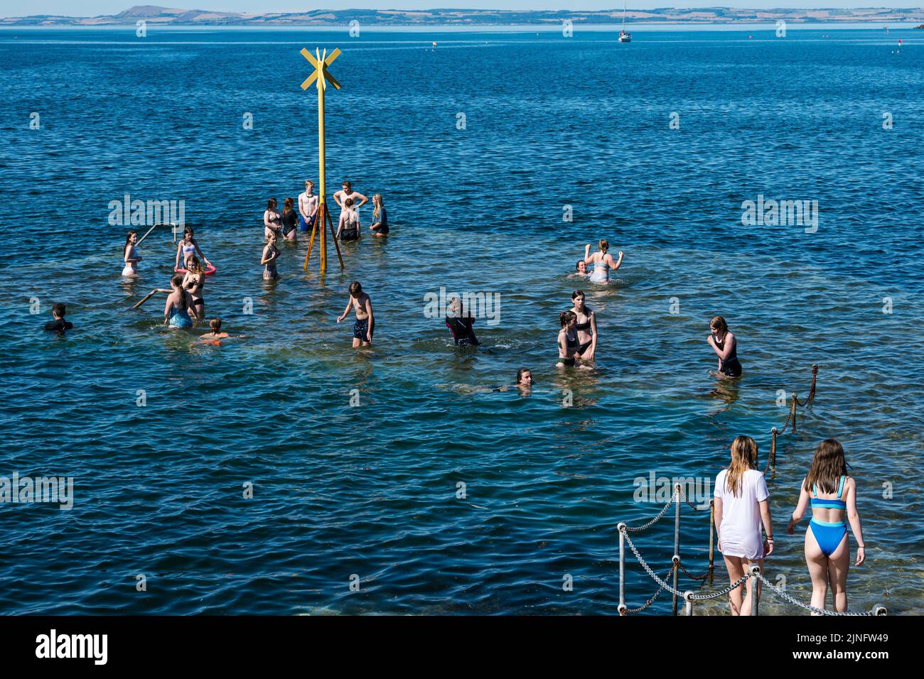 North Berwick, East Lothian, Scotland, UK, 11th August 2022. UK Weather: Keeping cool in the heat. With the temperature reaching up to 27 degrees, the seaside town offers opportunities to cool down. Children in swimsuits cooling off in the sea on the old pier as the tide rises and covers it in the Summer heatwave weather Stock Photo