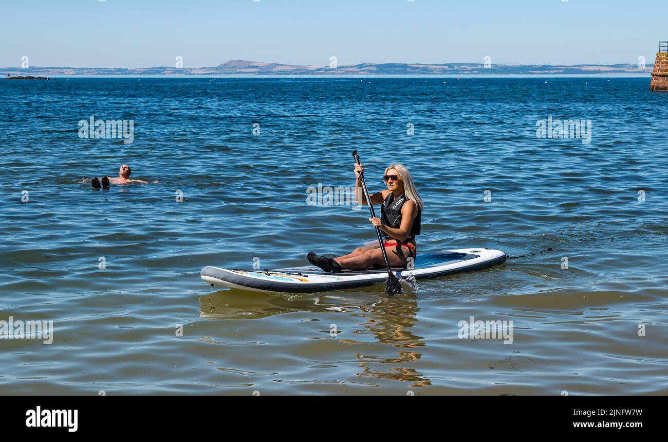 North Berwick, East Lothian, Scotland, UK, 11th August 2022. UK Weather: Keeping cool in the heat. With the temperature reaching up to 27 degrees, the seaside town offers opportunities to cool down. A woman paddle boarding in West Bay in the Summer heatwave weather Stock Photo