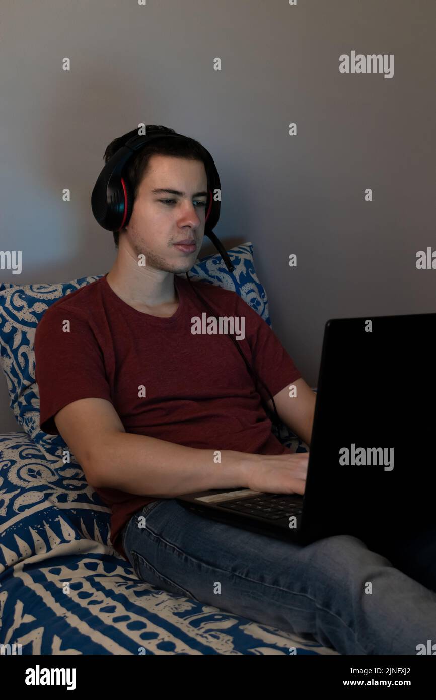 Teenager sitting on the bed playing video games on the laptop Stock