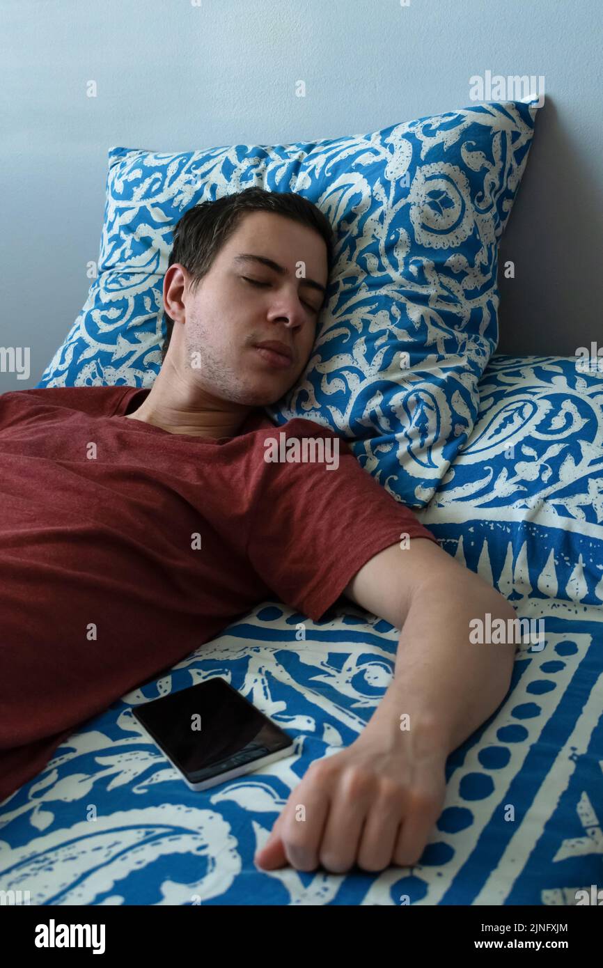 Millennial sleeping in bed near his mobile phone Stock Photo Alamy
