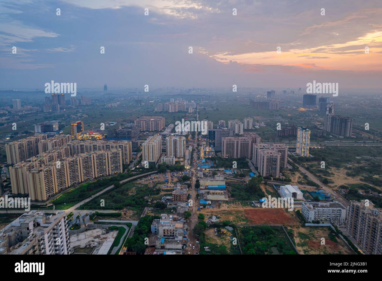 drone aerial shot showing busy traffic filled streets between skyscrapers filled with houses, homes and offices with a red sunset sky showing the Stock Photo