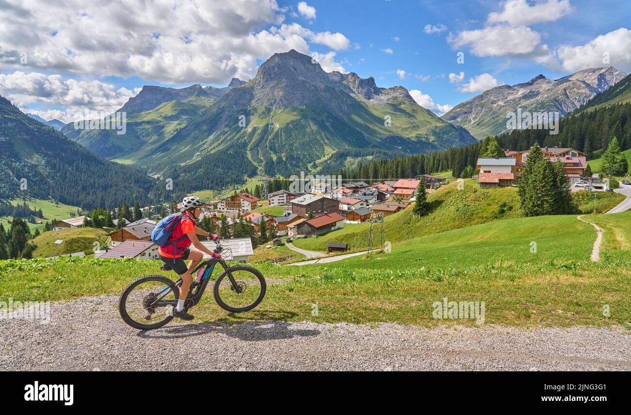 active senior woman, riding her electric mountain bike above famous village of Lech in the Arlberg area , Tirol, Austrian Alps Stock Photo