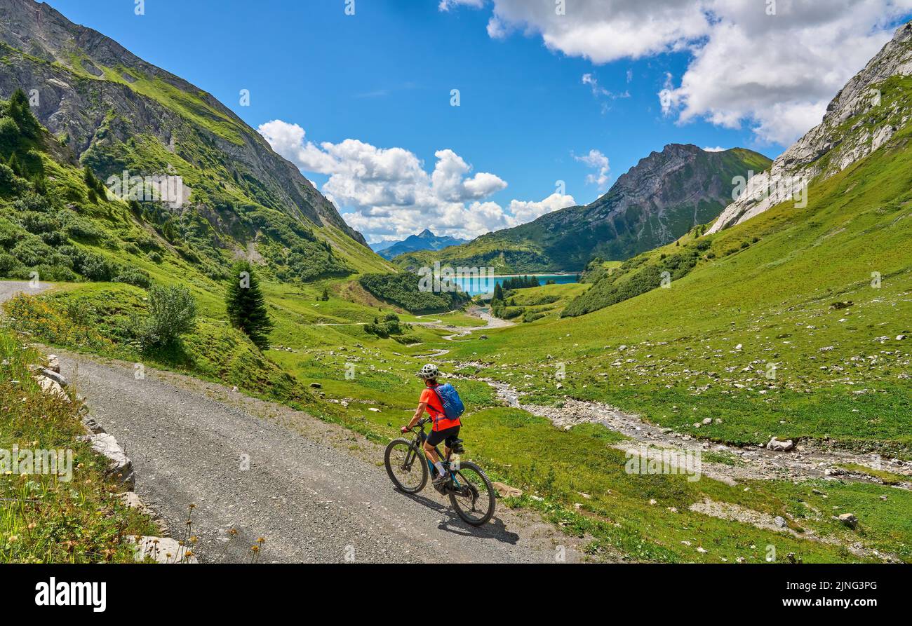 active senior woman, riding her electric mountain bike at Spuller Lake in the Arlberg area near the famous village of Lech, Tirol, Austrian Alps Stock Photo