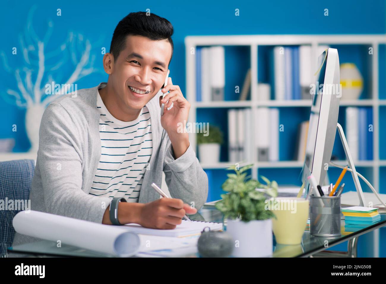Cheerful young architect calling on phone and taking notes Stock Photo