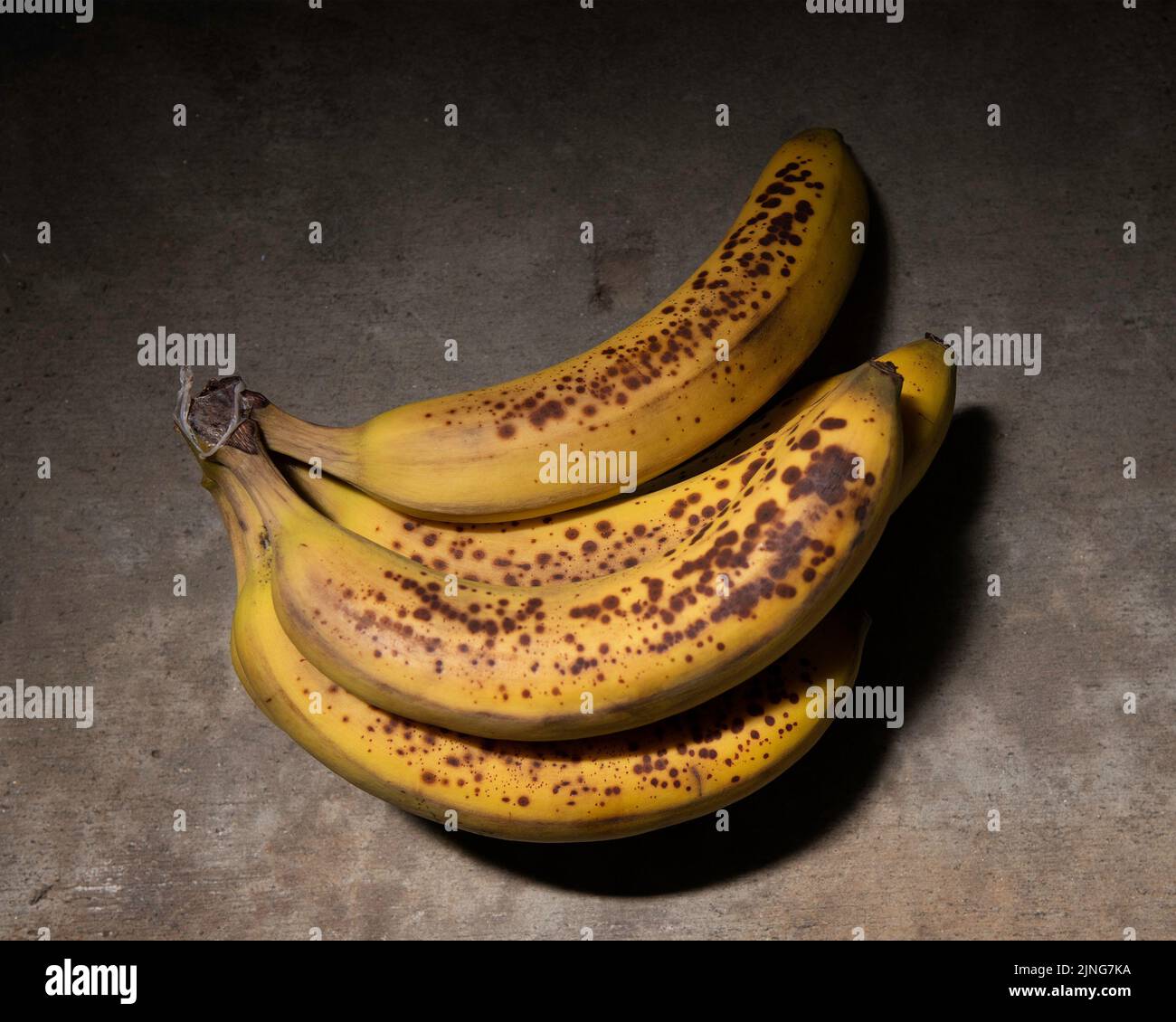 Close up of ripe mottled bananas against a concrete background. Stock Photo