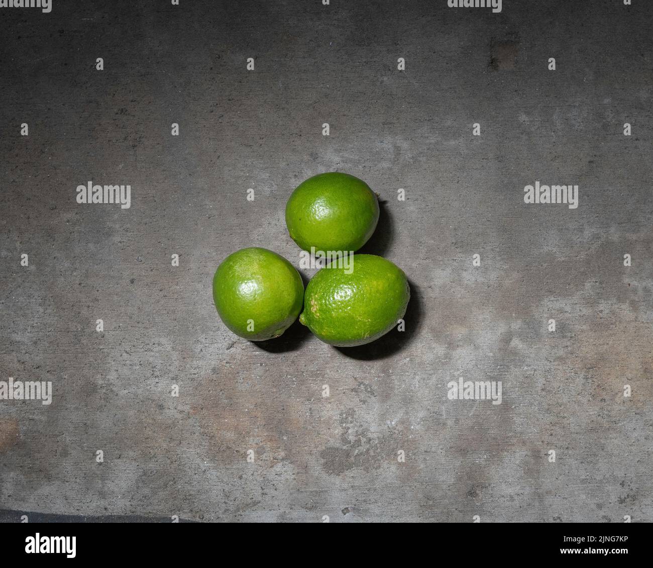 Close up of three bright green limes against a concrete background. Stock Photo