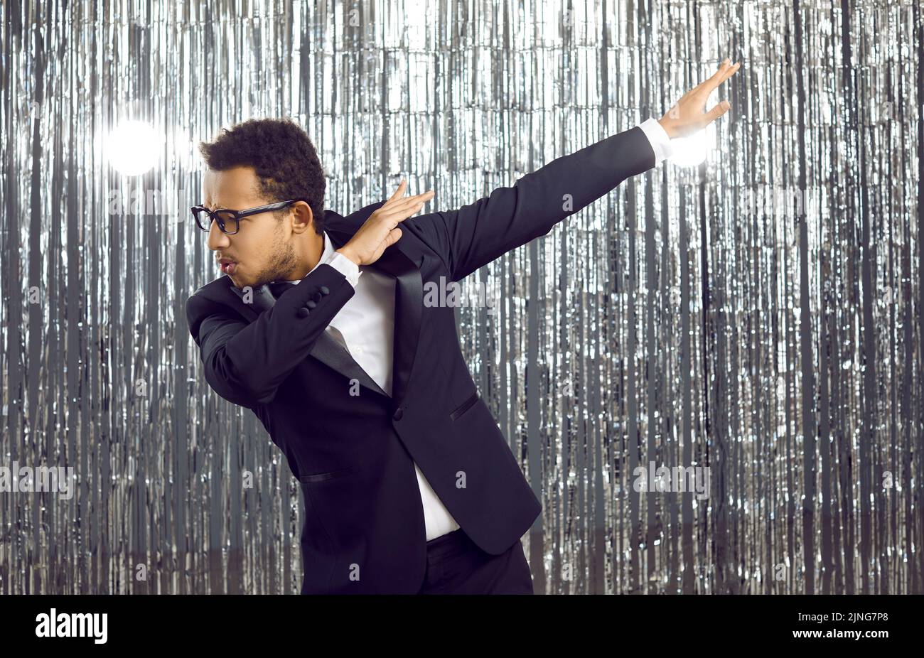 Happy confident black man in a tuxedo suit and glasses dancing and having fun at a party Stock Photo