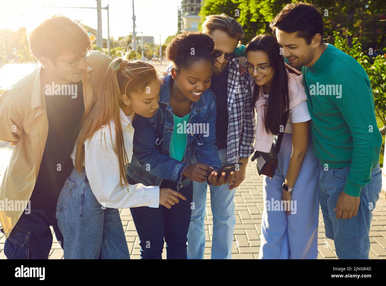 Multiracial young people bending over looking at screen of phone and ...