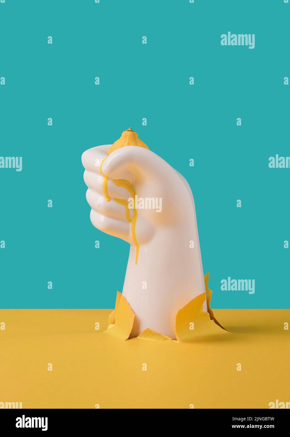 Ceramic hand squeezing lemon with juice dripping. Nature destruction surreal concept. Stock Photo
