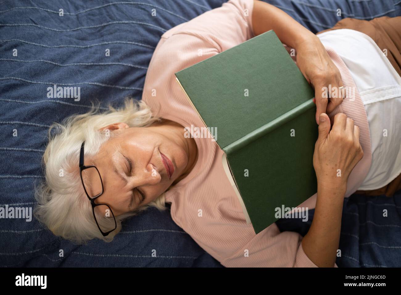 senior woman lying on sofa and sleeping with book. Top view Stock Photo