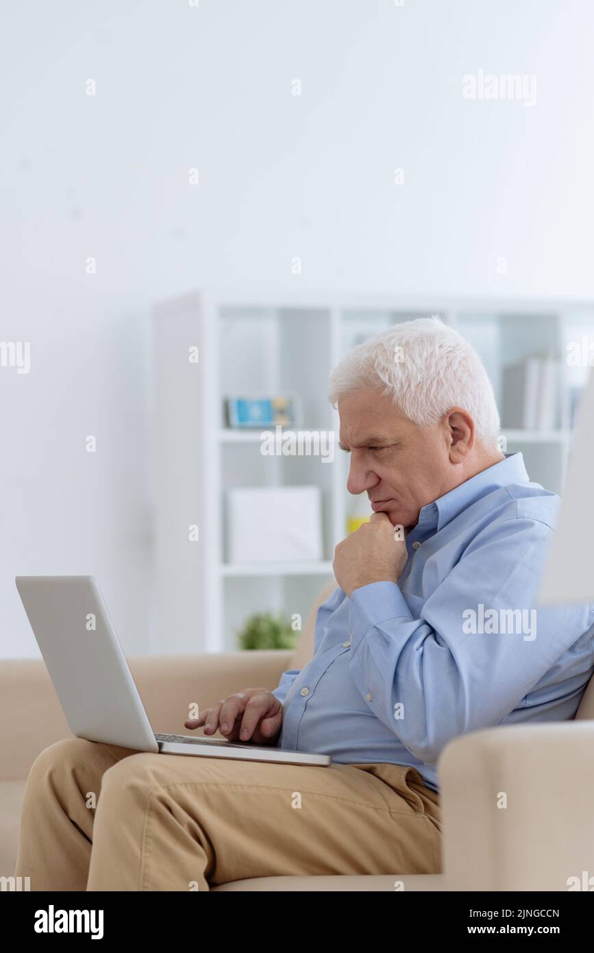 Concentrated aged man reading information on laptop screen Stock Photo