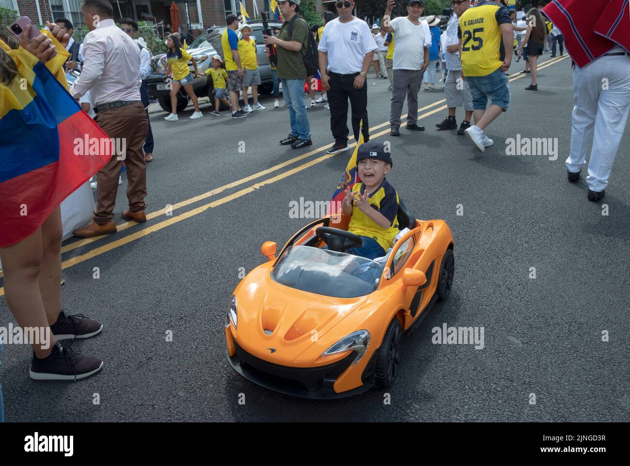 An unhappy young Ecuadorian boy rides his electric car on 69th Street just prior to the Ecuadorian Parade NYC 2022 in Jackson Heights, Queens, NYC. Stock Photo