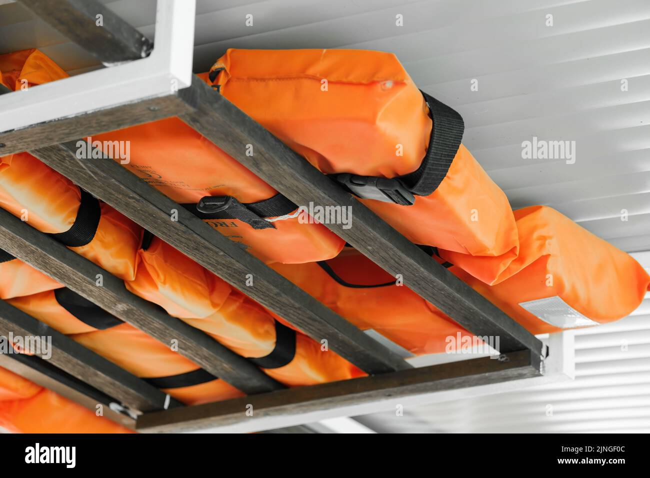 Orange life jackets for extremal situations on water attached to boat ceiling. Life jackets for group of tourists for protection and safety closeup Stock Photo