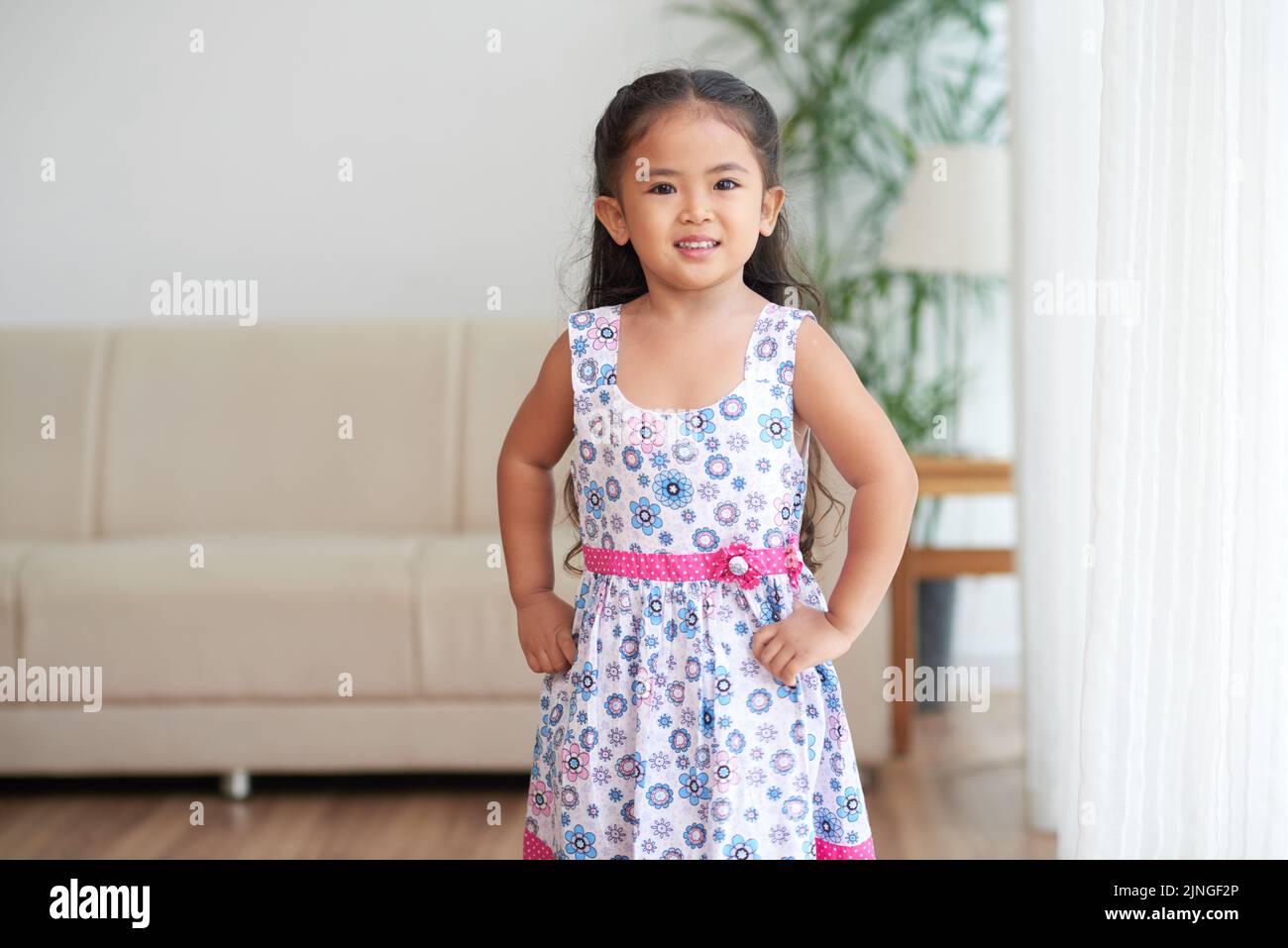 Smiling girl standing with hands on her hips and looking at camera ...