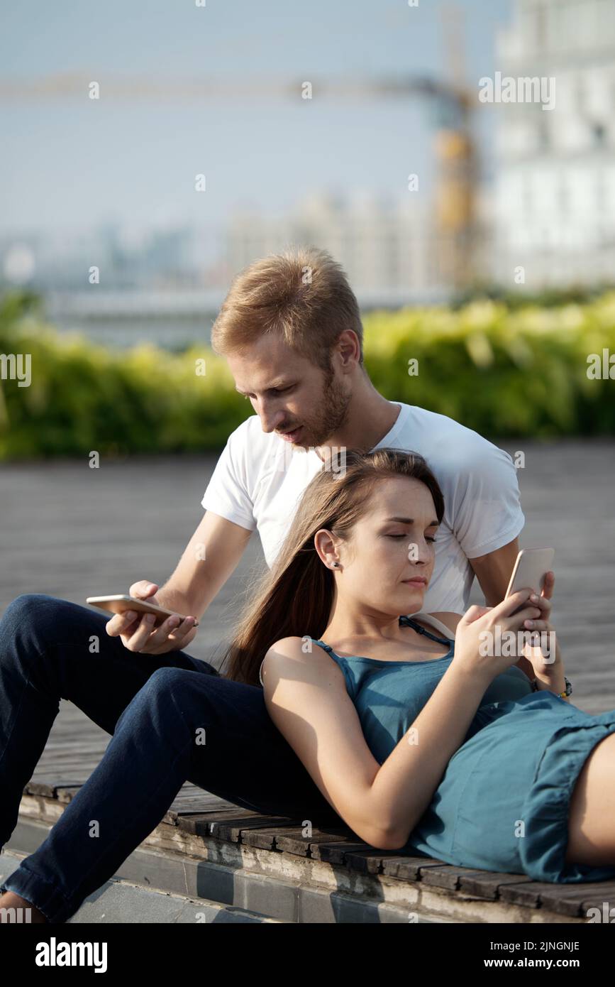 Young couple using smartphones while relaxing together outdoors Stock Photo