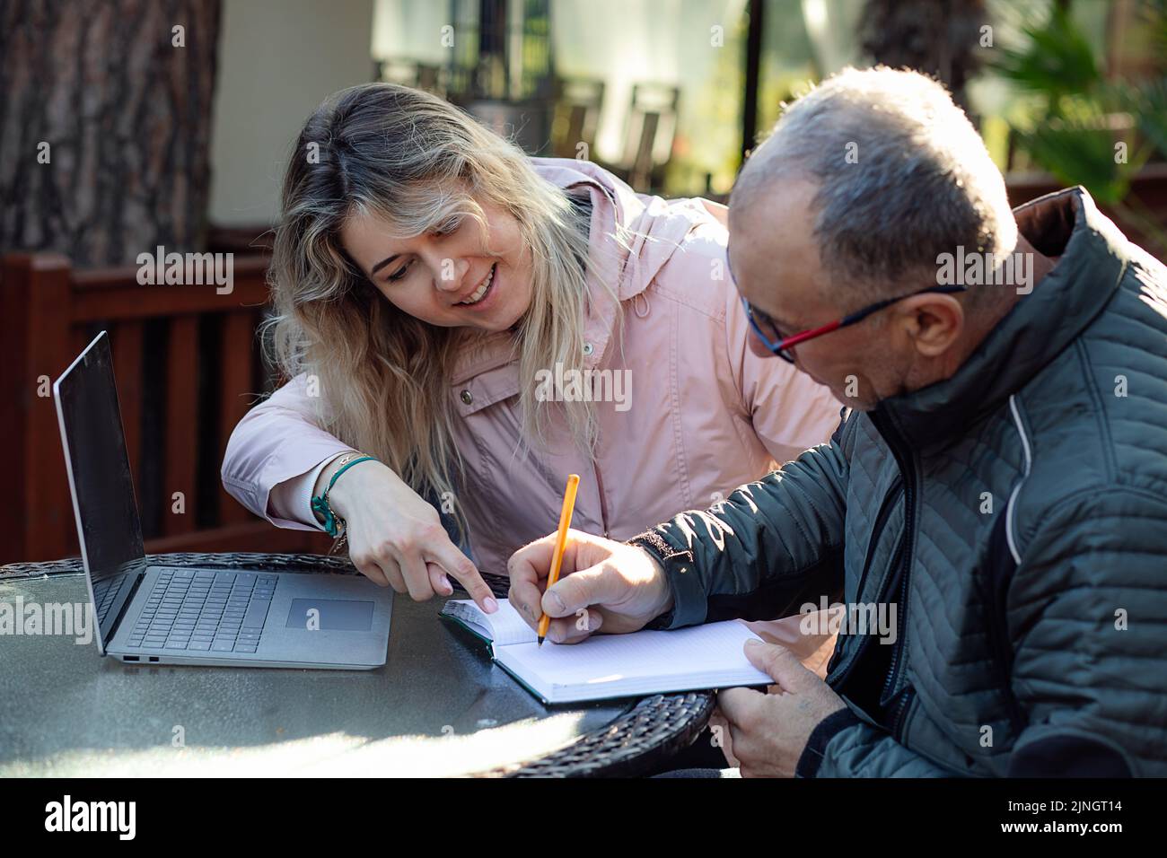 Portrait of young smiling woman daughter coach trainer sitting, talking to middle-aged man father, pointing at mistakes. Stock Photo