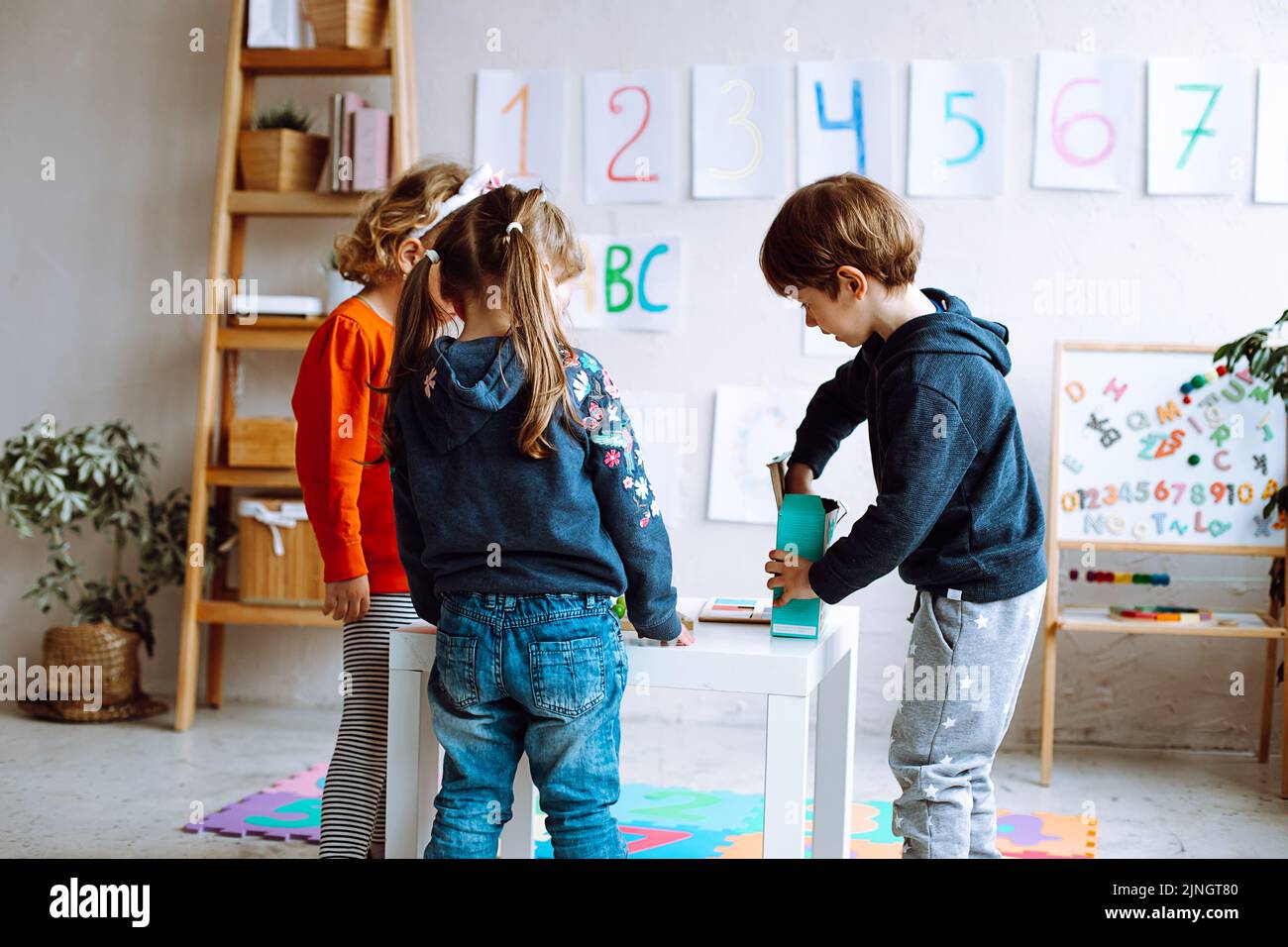 Group of wonderful children preschoolers studying playing in bright classroom. Pupils standing around white table. Stock Photo