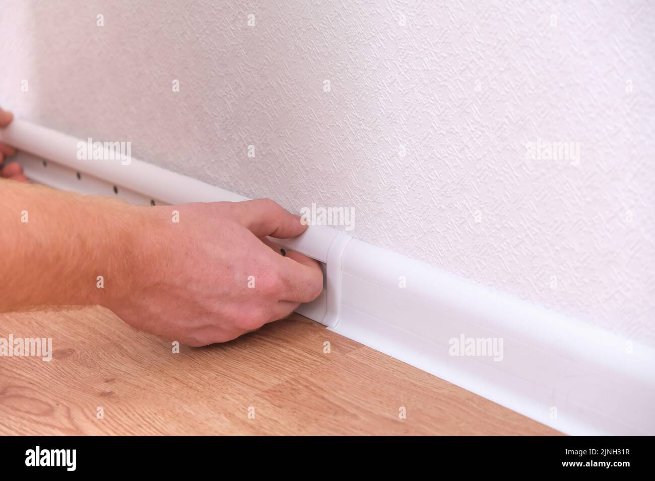 A man installs a floor skirting board. Fixing the plastic skirting