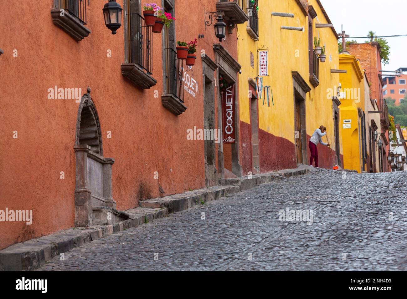 A woman sweeps the walkway on Calle Cuadrante lined with colorful Spanish colonial style buildings in the historic city center of San Miguel de Allende, Mexico. Stock Photo