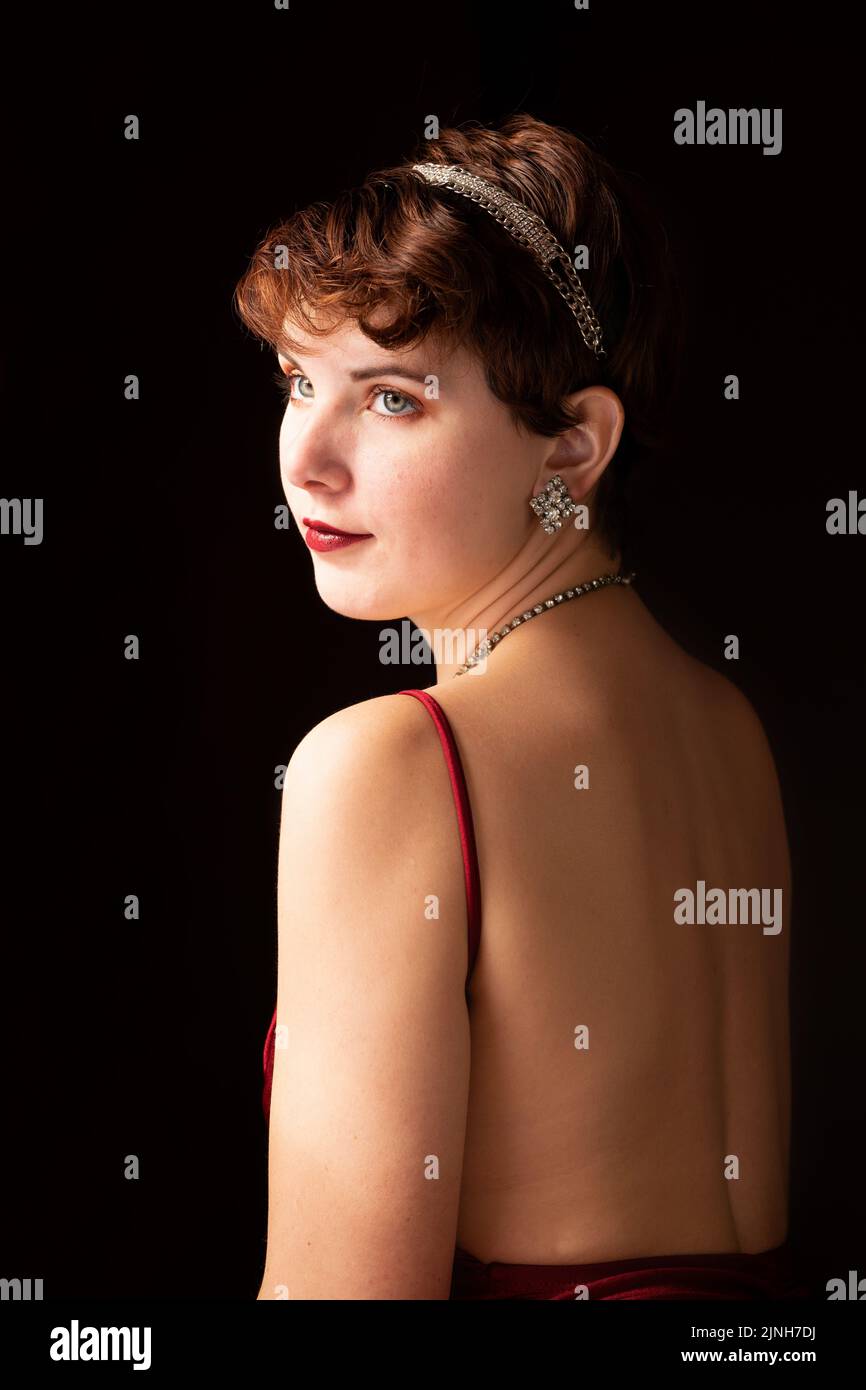 Self-portrait. Window-lit portrait of a woman with short hair wearing a red gown and vintage jewelry. Red lips, hazel eyes, brunette Stock Photo
