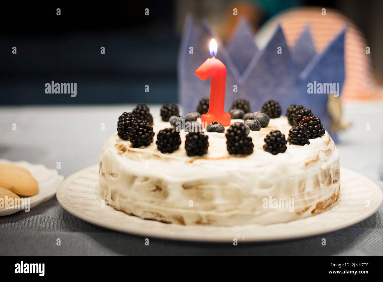 Simple homemade birthday cake for one year old baby party, with berries and red candle. Background with copy space. Stock Photo