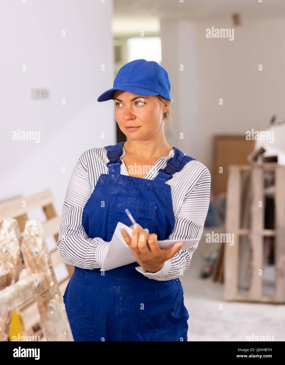 Female foreman in blue workwear making task list in building under construction Stock Photo