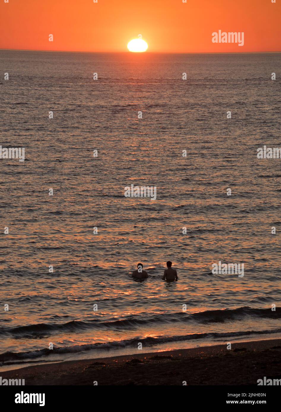 Couple at sunset enjoying the sun and swimming in the sea under heatwave on beach in Aberystwyth,Ceredigion,Wales,UK Stock Photo